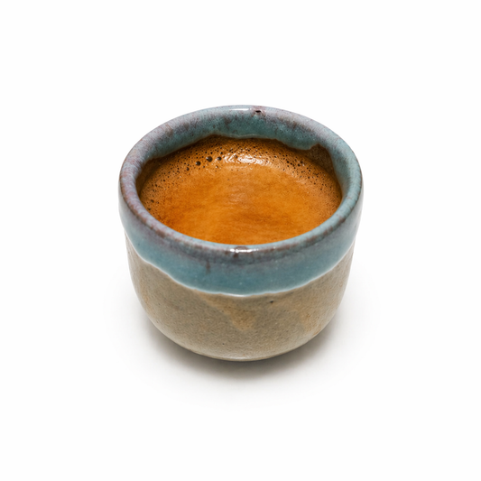 Ceramic cup with a blue rim and brown interior filled with a dark liquid on a white background