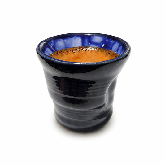 Blue ceramic cup with a textured surface containing a brown liquid on a white background