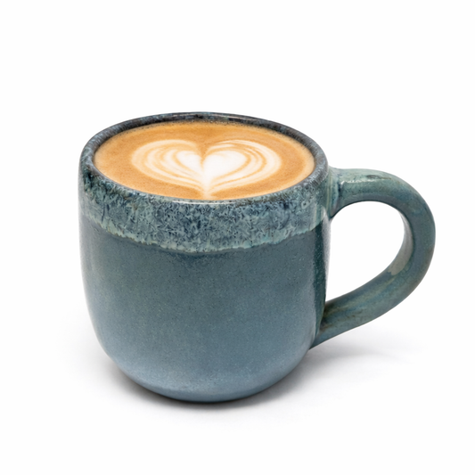 Blue ceramic mug with a heart-shaped latte art on a white background
