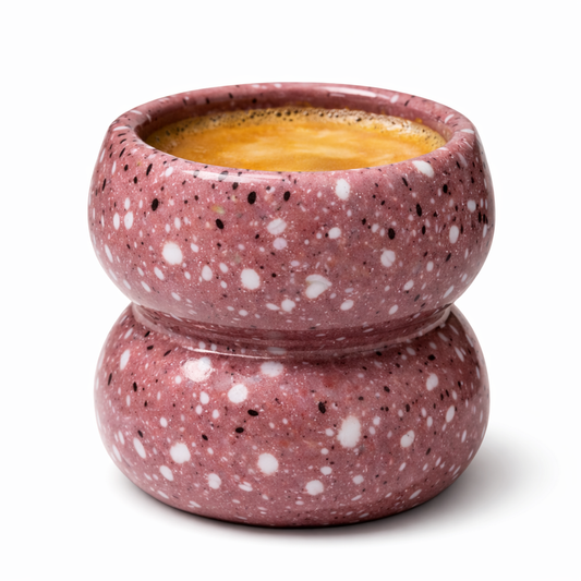 Speckled pink ceramic bowl with a white interior filled with a yellowish liquid on a white background