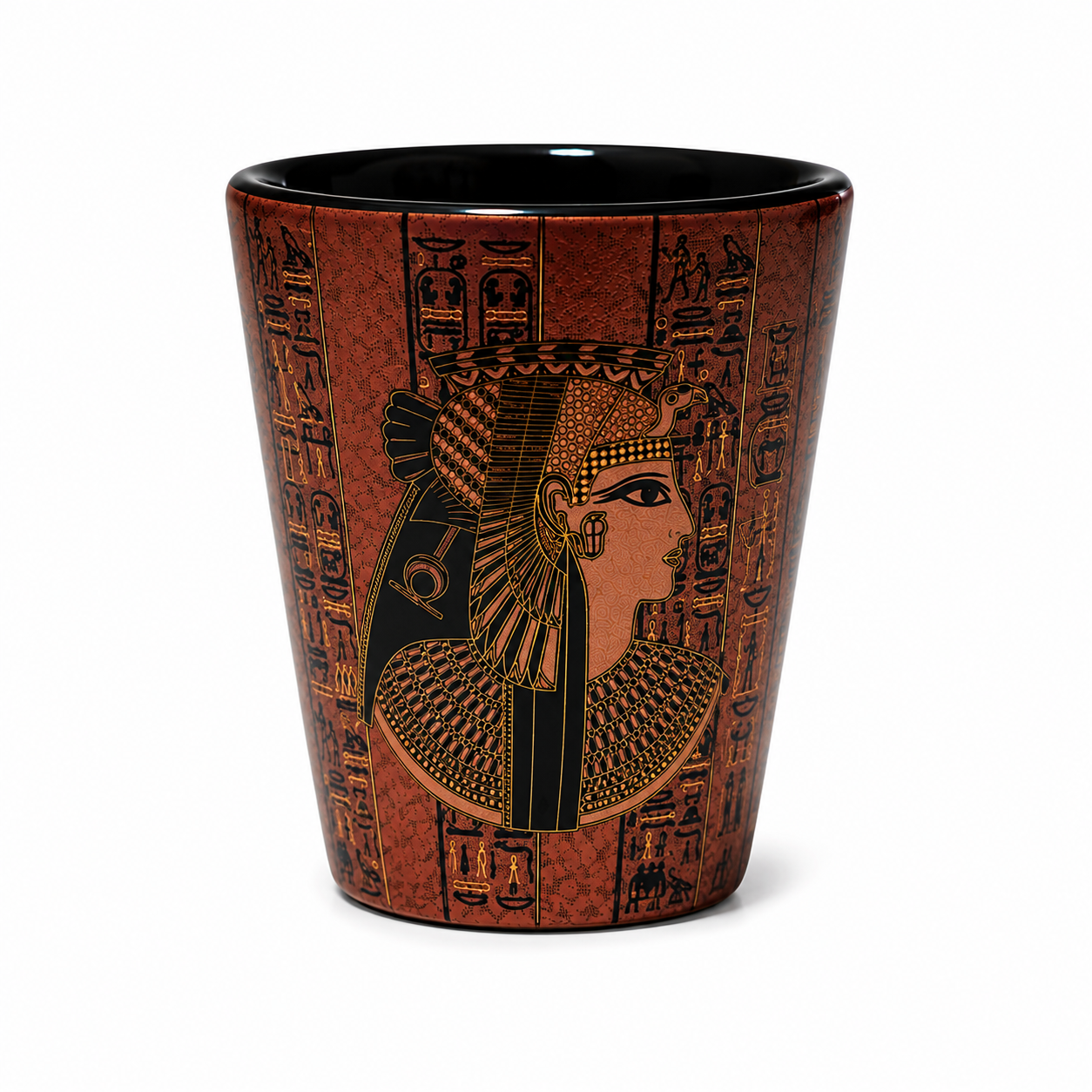A brown ceramic shot glass featuring an Egyptian portrait of a queen with a headdress and hieroglyphic designs printed on a textured brown background, with a black interior.