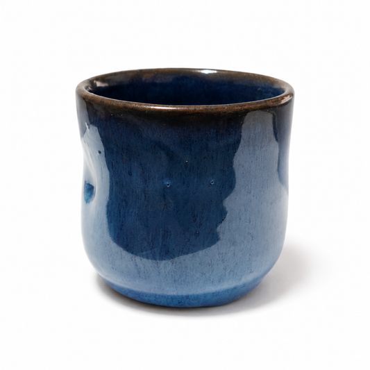 A small handmade ceramic cup with a glossy dark blue glaze and a contrasting dark brown unglazed rim, shown on a plain white background.