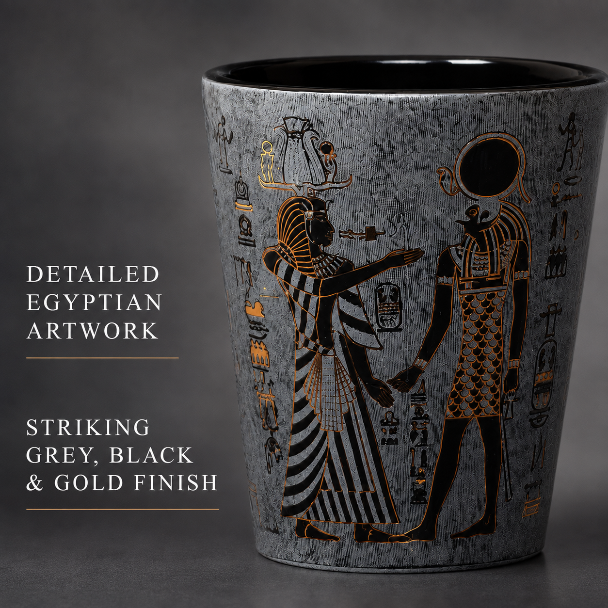 A textured grey ceramic cup featuring black and gold Egyptian artwork with figures and hieroglyphs, shown against a dark grey background with text overlays describing the detailed finish.