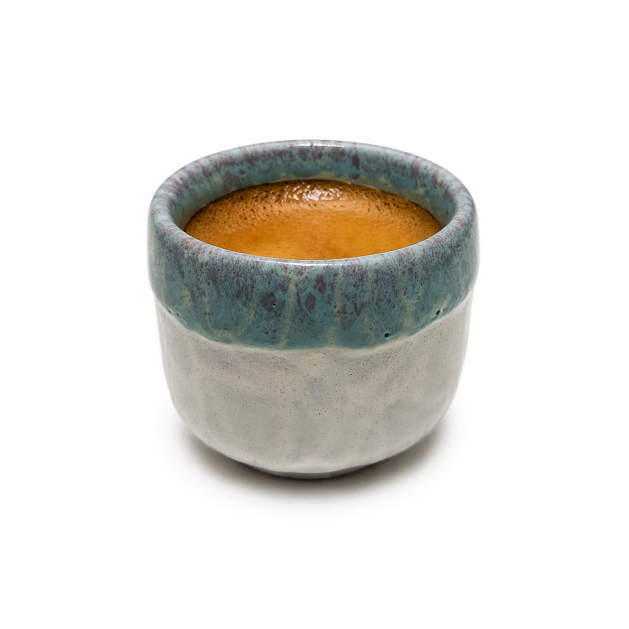 Ceramic cup with a blue rim and gray base containing a brown liquid on a white background