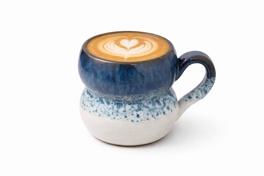 Blue speckled ceramic mug with a heart-shaped latte art on a white background