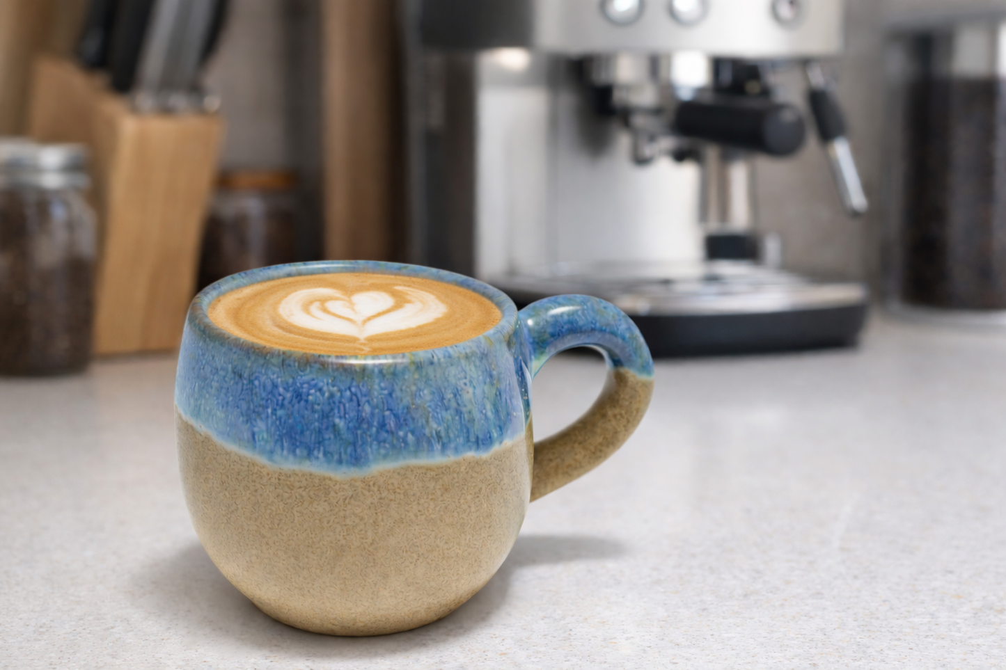 Ceramic mug with a layered design containing a coffee drink with latte art in a kitchen setting.