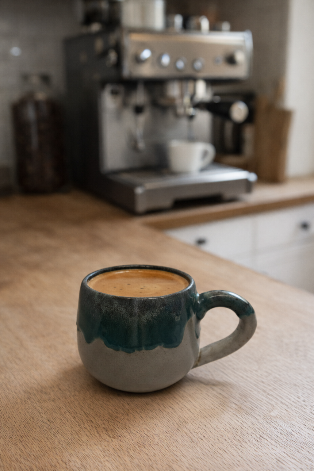 Ceramic mug with coffee in front of an espresso machine on a wooden counter.