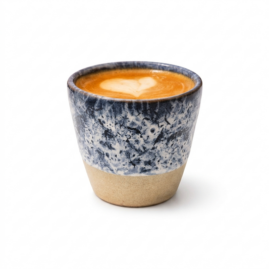Speckled blue and beige ceramic cup with a heart-shaped latte art on a white background