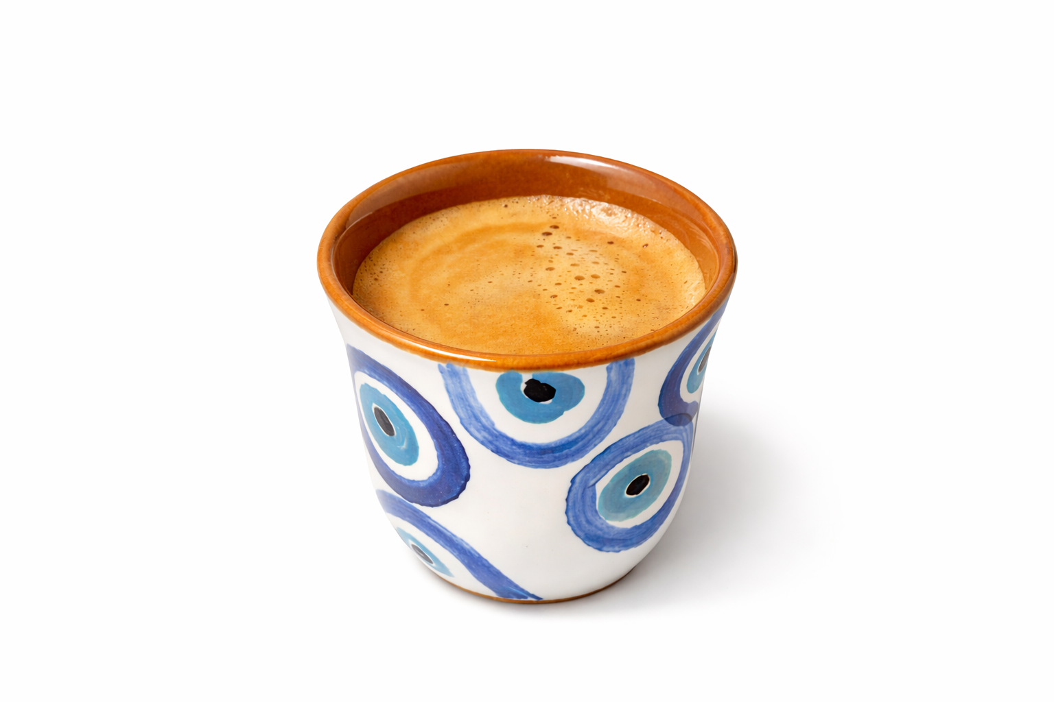 Ceramic cup with blue evil eye design filled with espresso on a white background