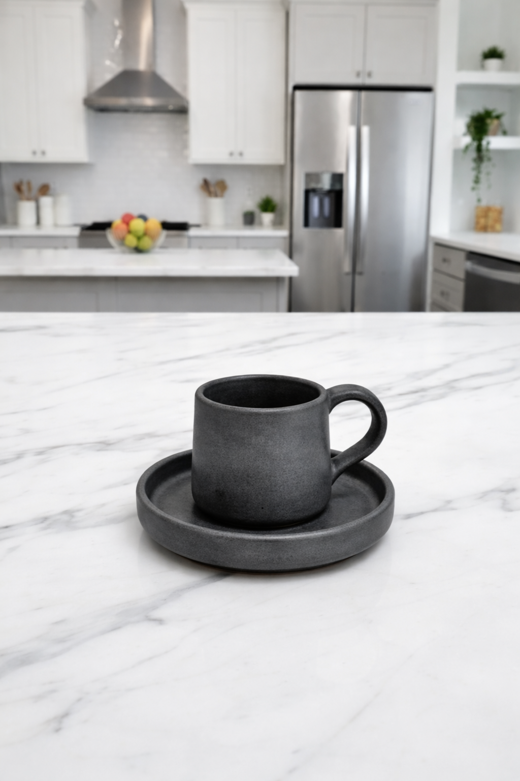 Charcoal black mug and saucer set on a marble countertop with a kitchen in the background