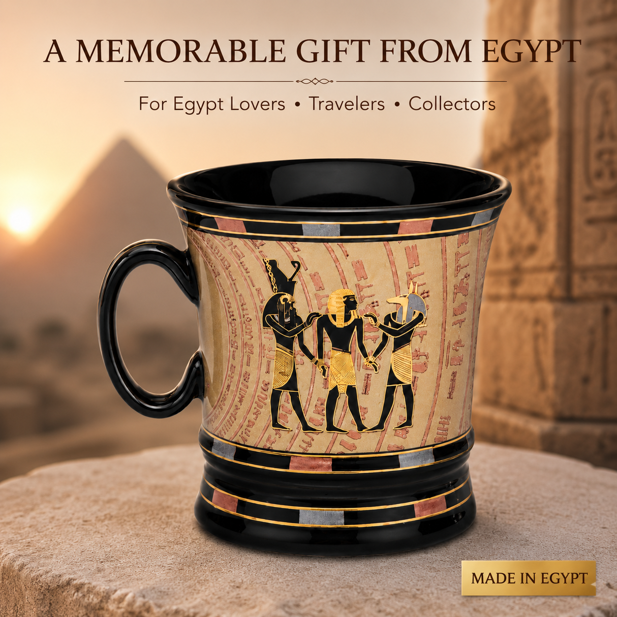 A ceramic mug with an Egyptian theme, featuring a black handle and rim, a beige body with hieroglyphic figures and script, and gold accents. The mug is set on a stone pedestal with a blurred background of pyramids and ancient ruins under a warm sunset sky.