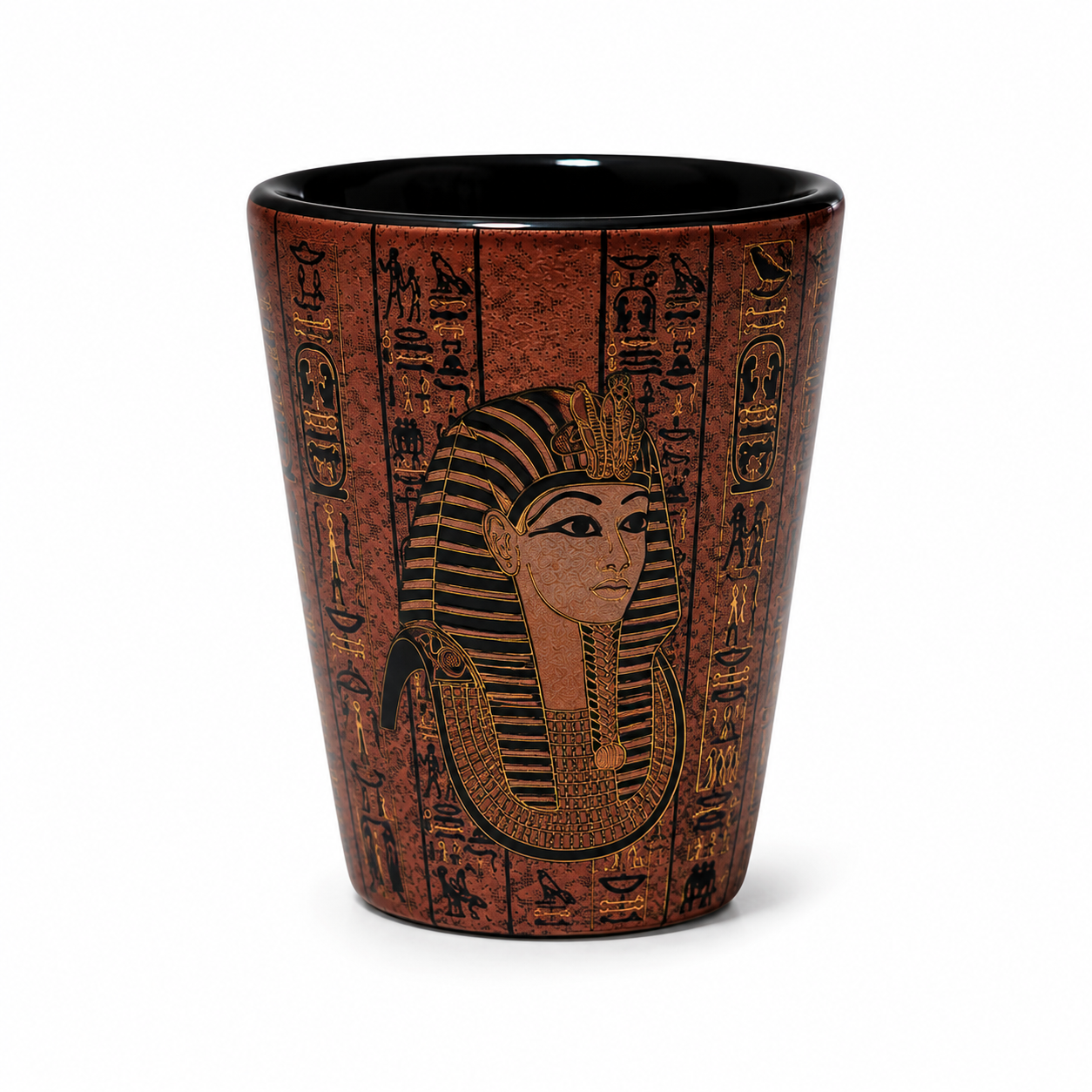 An Egyptian-themed shot glass featuring a detailed relief design of Pharaoh Tutankhamun and hieroglyphs on a reddish-brown textured background, with a glossy black interior, set against a plain white background.