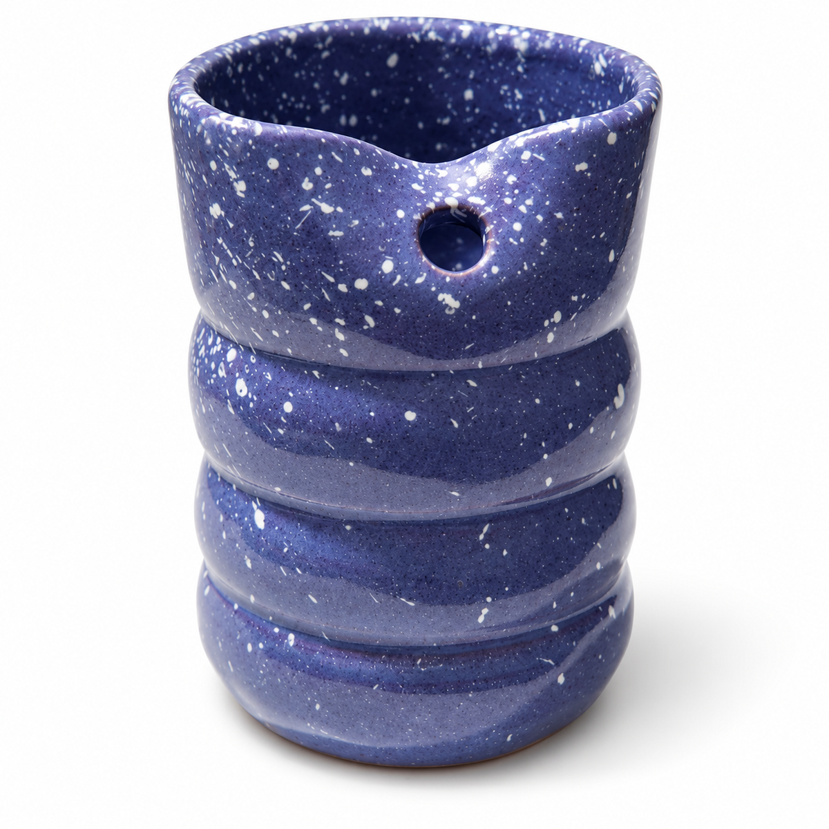 A ceramic cup with a wavy, ribbed body and a small hole on the side, glazed in a deep blue with white speckles, on a white background.