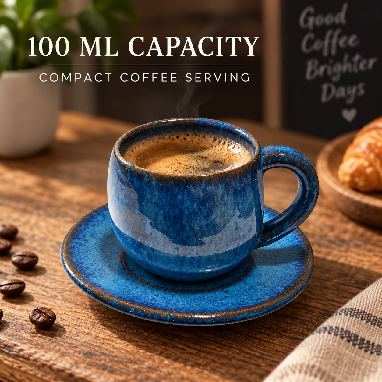 A small blue ceramic espresso cup with matching saucer on a wooden table, filled with coffee and shown with text reading '100 ML CAPACITY' and 'COMPACT COFFEE SERVING'. Coffee beans, a croissant, and a plant are softly blurred in the background.