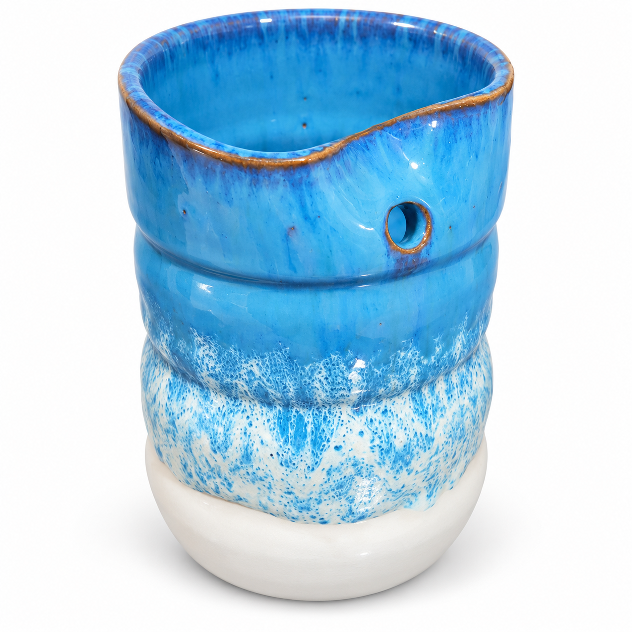 A handmade ceramic vessel with a wavy, ribbed design, featuring a vibrant blue glazed upper section, a speckled blue and white middle section, and a solid white base. It has a small pouring spout on one side and a small circular hole on the front.