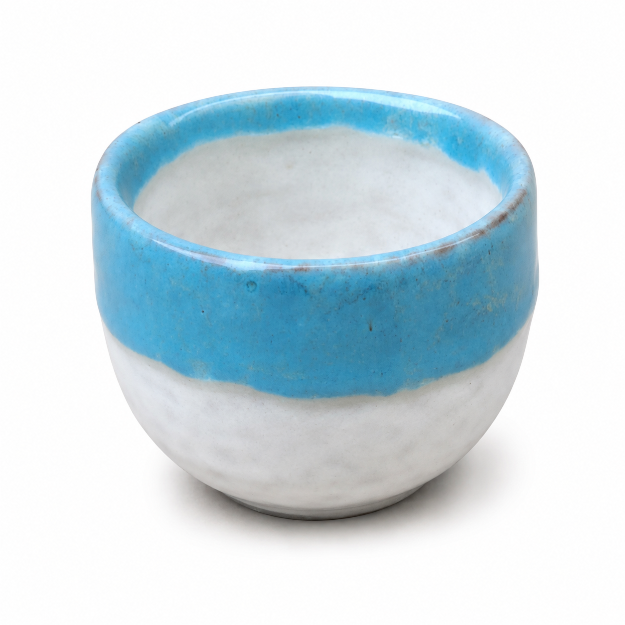 A small handmade ceramic cup with a glossy blue glazed rim and a matte white glazed body, shown on a clean white background.