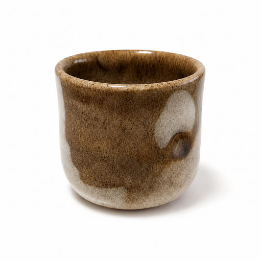 A small handmade ceramic cup with a brown and beige glaze, photographed on a clean white background.