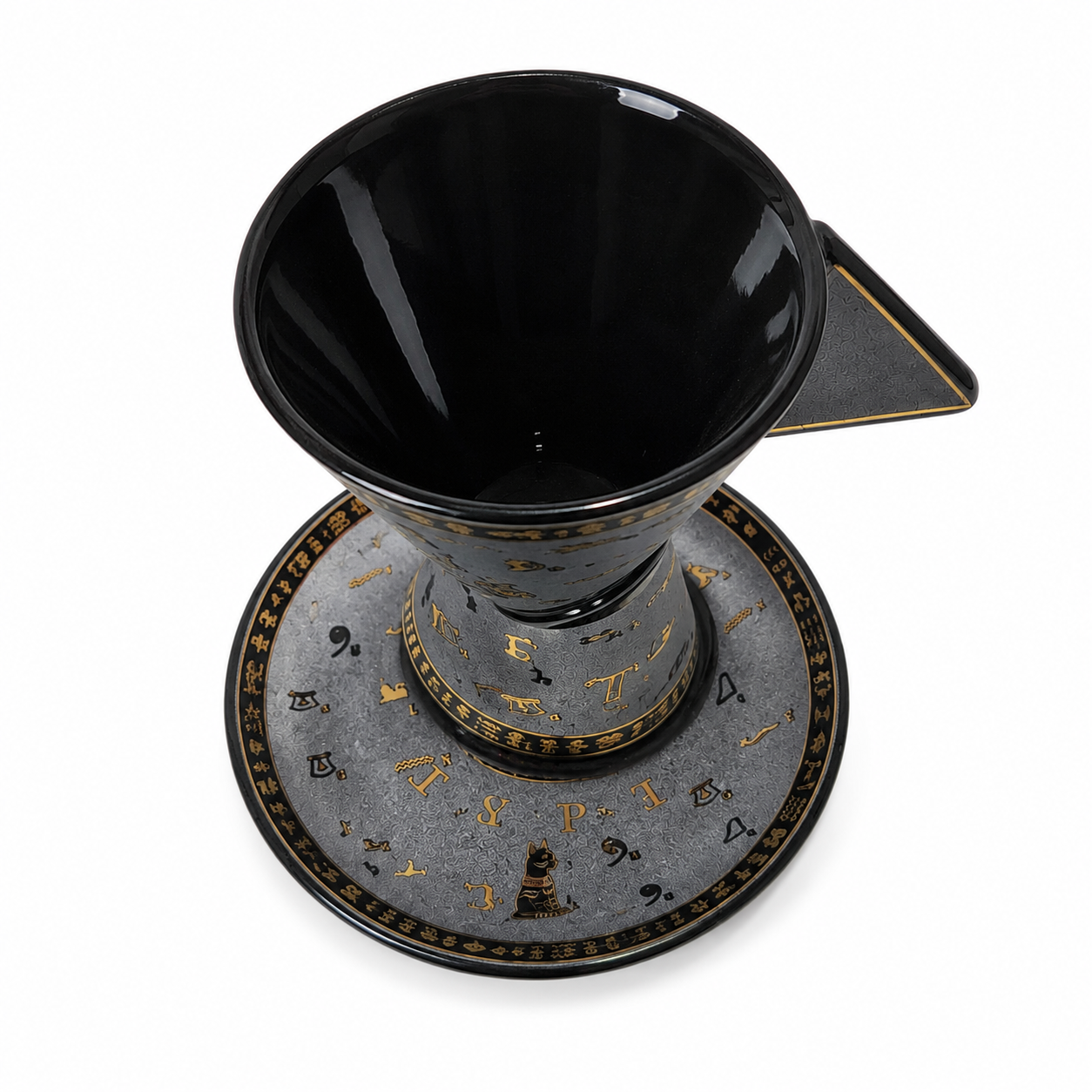 A black ceramic pour-over coffee maker with a matching saucer, decorated with gold astrological symbols and a small central figure. The cone-shaped filter sits in the saucer, and a small triangular spout extends from the side.