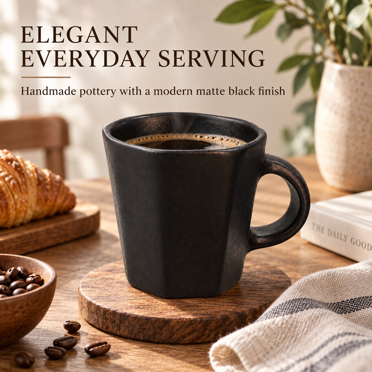 A matte black ceramic coffee mug filled with black coffee, set on a wooden coaster on a rustic table with a croissant, coffee beans, a book, and a plant in the background. Text at the top reads 'ELEGANT EVERYDAY SERVING' and 'Handmade pottery with a modern matte black finish.