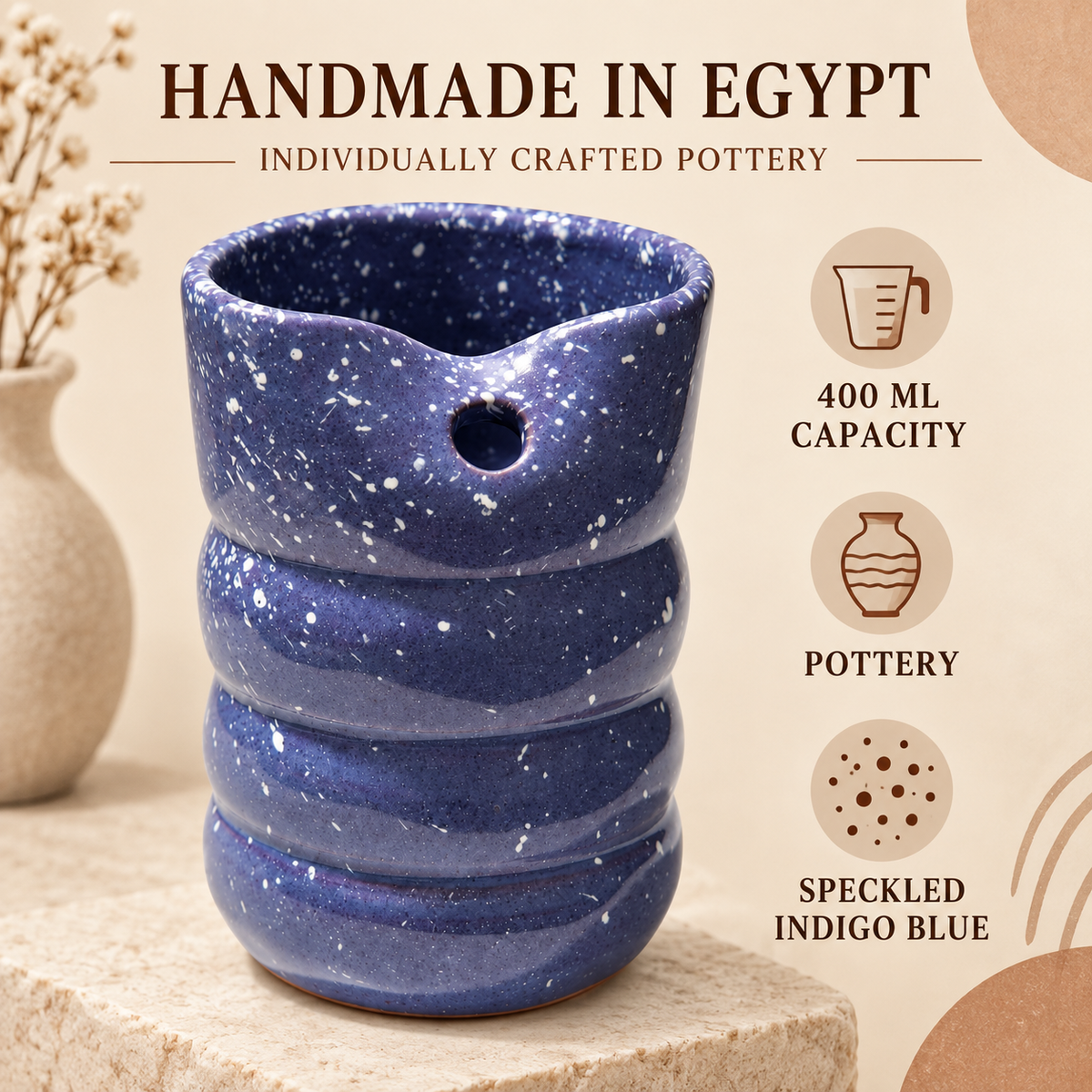 A handmade Egyptian pottery pitcher in speckled indigo blue, displayed on a stone pedestal with decorative props and text overlays highlighting its 400 ml capacity and speckled finish.