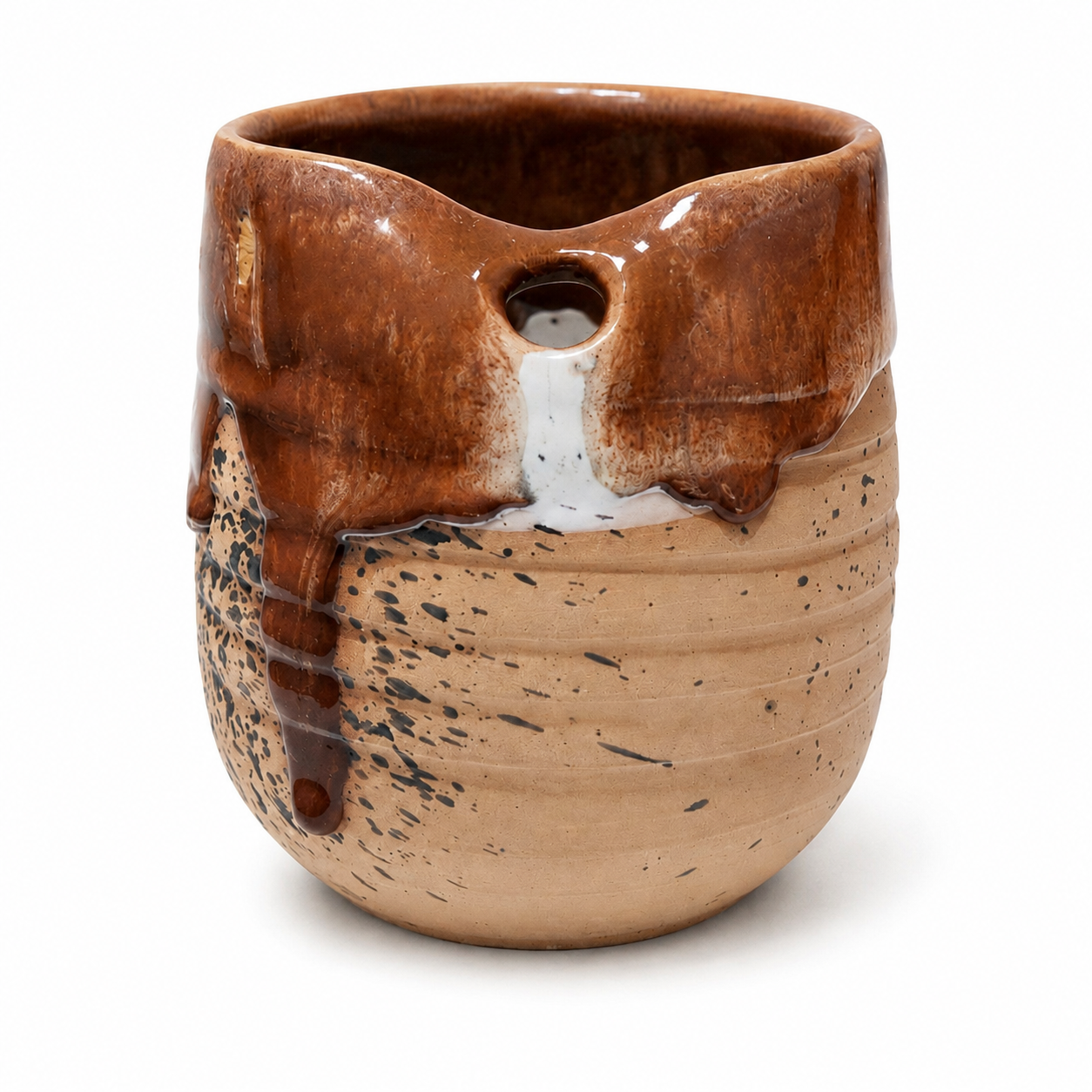 A handmade ceramic pitcher with a glossy brown dripped glaze on the top half and a speckled beige clay body on the bottom half, featuring a small pouring spout and a small hole near the rim.