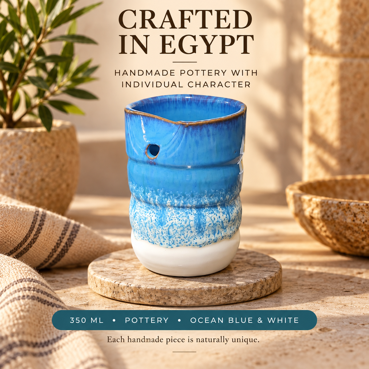 A handmade ceramic potter's wheel in ocean blue and white glaze, displayed on a stone coaster with a burlap cloth, potted plant, and stone bowls in a warm, rustic setting. Text overlays read 'CRAFTED IN EGYPT' and '350 ML • POTTERY • OCEAN BLUE & WHITE'.