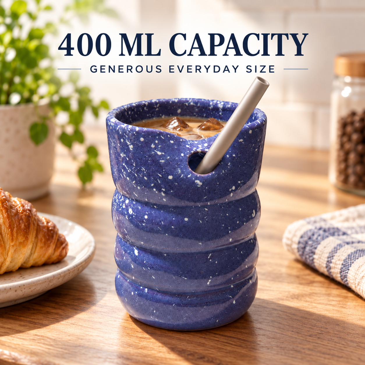 A blue speckled ceramic mug with a built-in straw and a small side hole, shown on a wooden table with coffee inside. Text at the top reads '400 ML CAPACITY' and 'GENEROUS EVERYDAY SIZE.