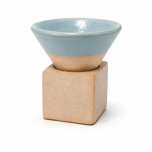A ceramic coffee cup with a light blue glazed top and a natural beige unglazed base, resting on a matching square ceramic coaster against a white background.